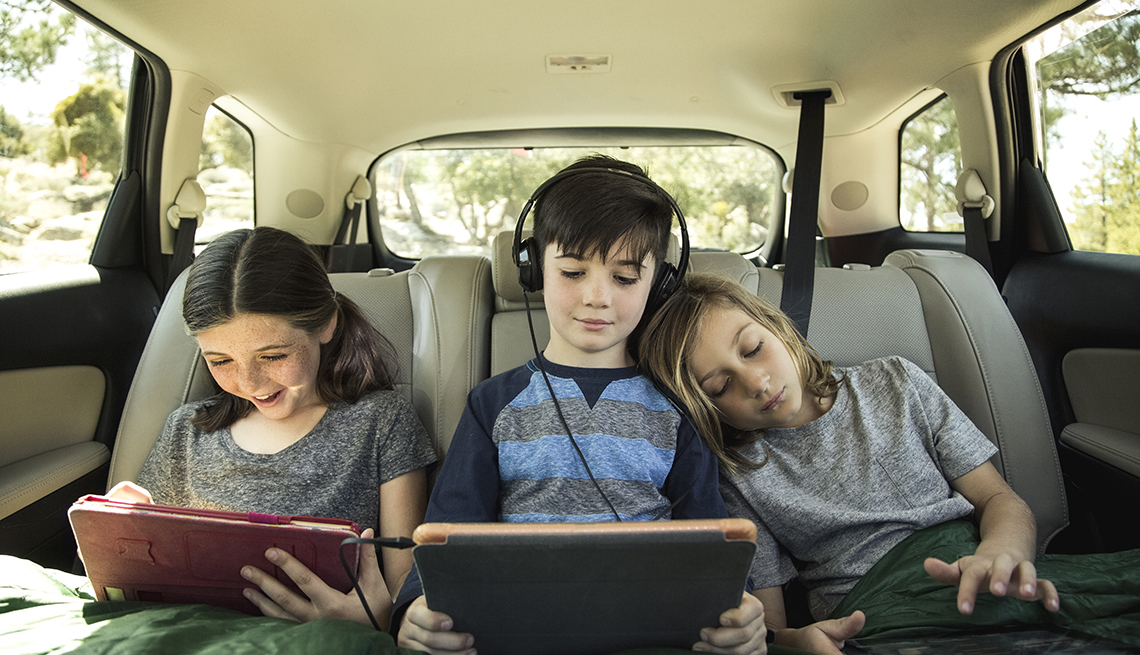 children in the back of a vehicle looking at tablets