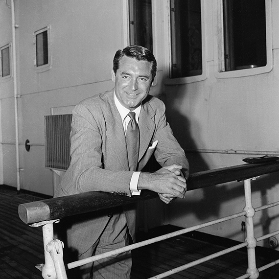 a black and white photo of actor Cary Grant in a suit with his hands resting on a rail