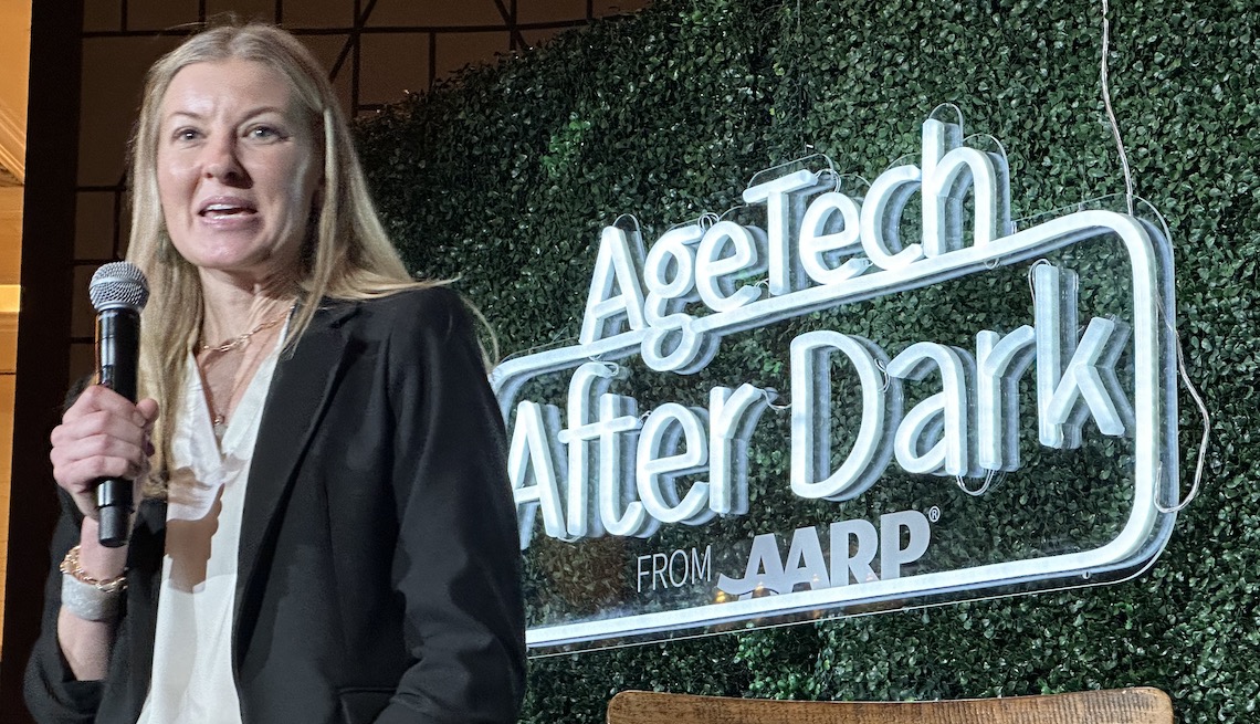 onward co-founder kim petty talks into a microphone with the words agetech after dark from aarp in the background
