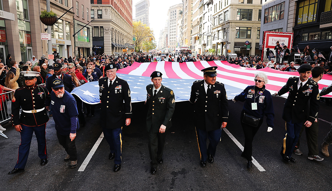 Grupo de veteranos carga la bandera de Estados Unidos mientras camina en la calle.