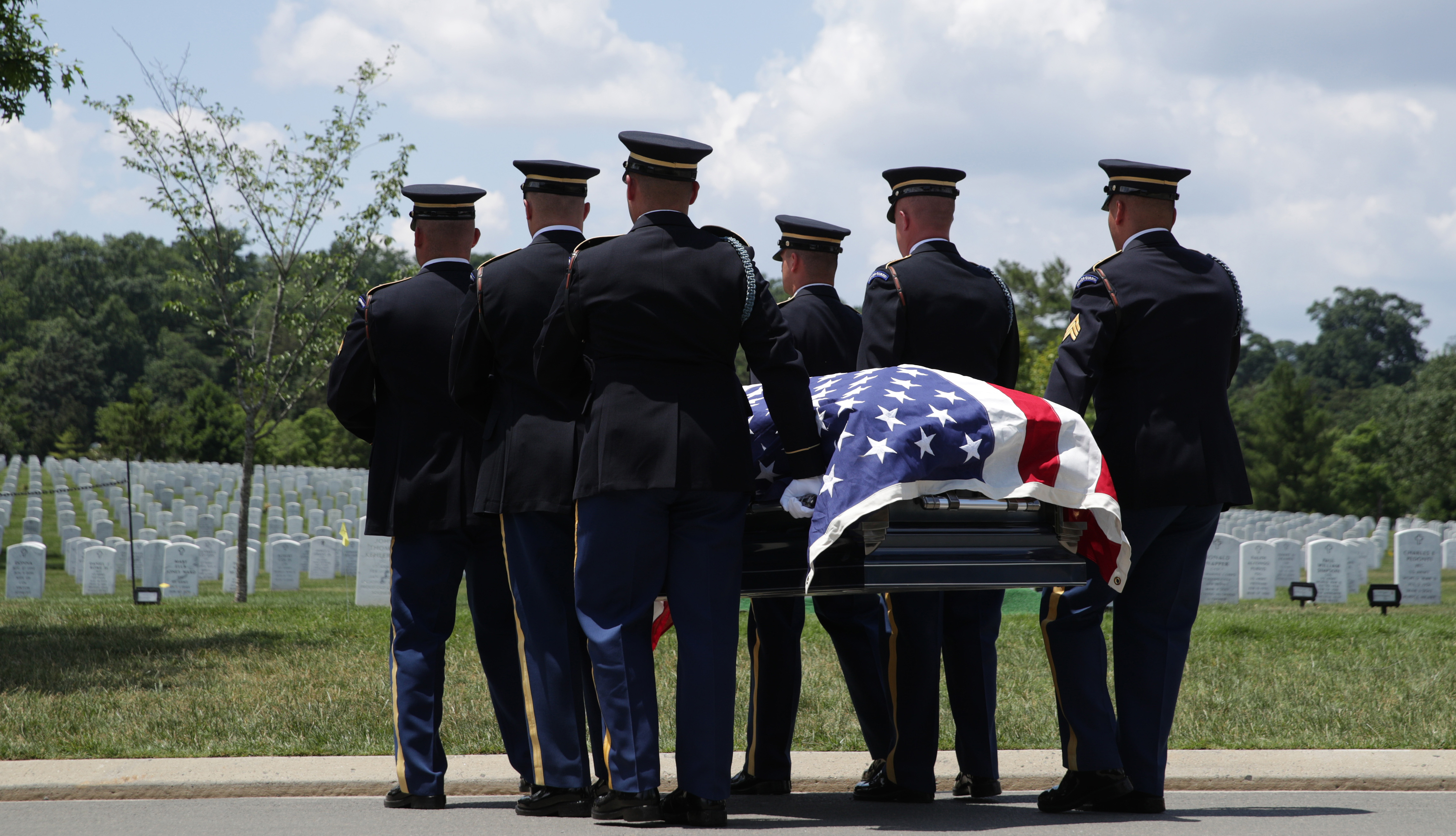 Hombres en uniforme llevan un ataúd envuelto en la bandera estadounidense en un cementerio