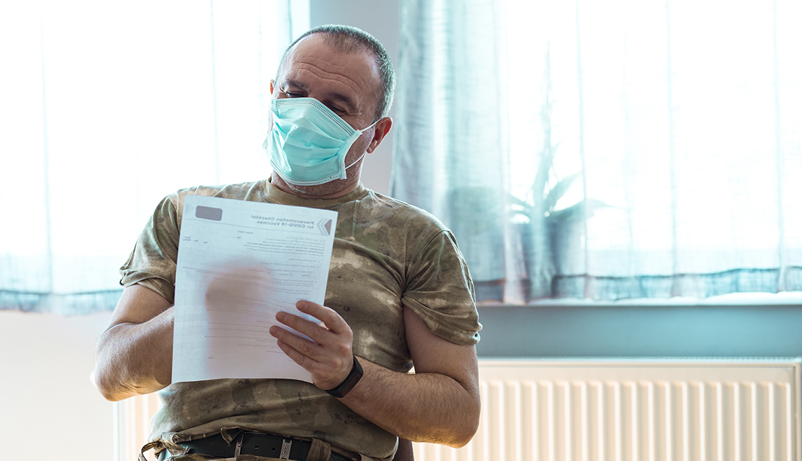 Un veterano militar con una máscara quirúrgica llena un formulario de vacunación contra la COVID-19