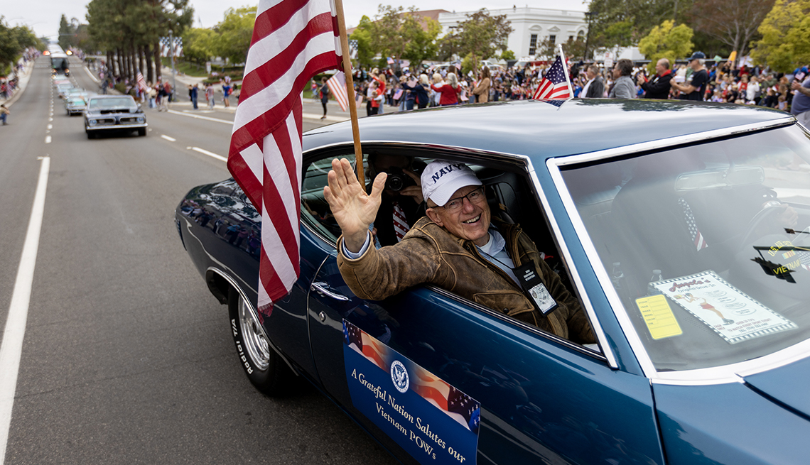 Charlie Plumb waves to crowds while riding in a classic car during a parade to honor American prisoners of war in Vietnam in May.