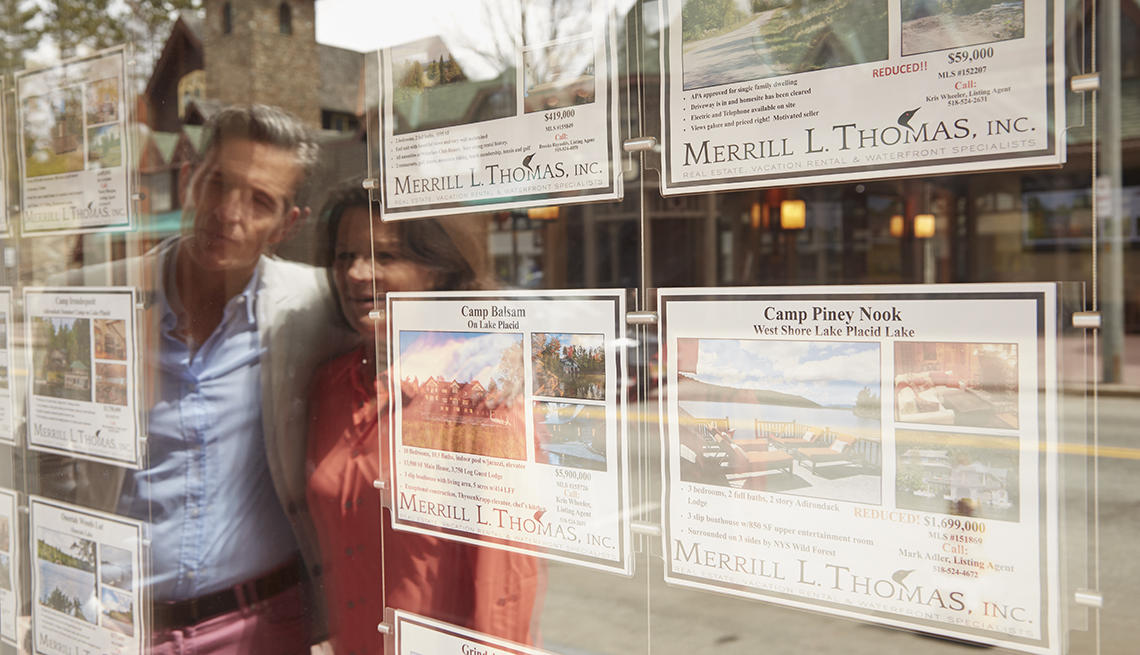 A man and woman looking at housing ads posted on a window. 