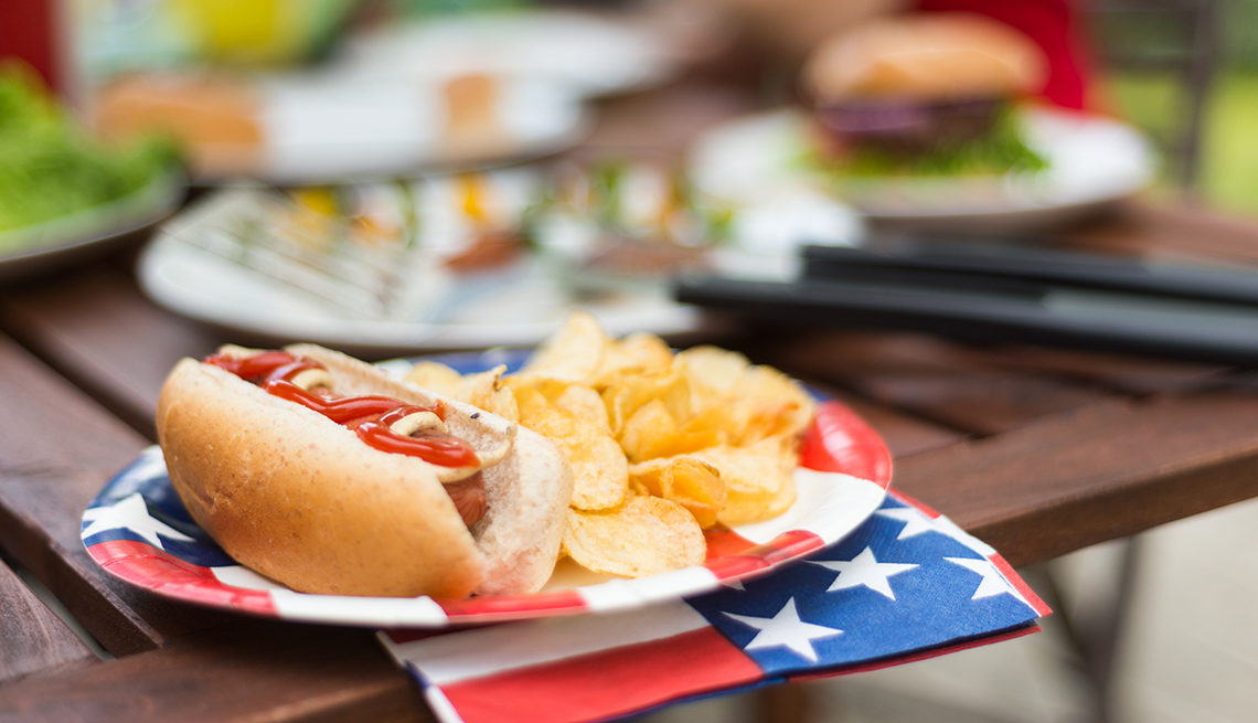 Hot Dog with potato chips at Fourth of July BBQ with people and other picnic items in the background. Influenced by the current trend in food photography of showing food in the foreground and lifestyle imagery out of focus in the background.