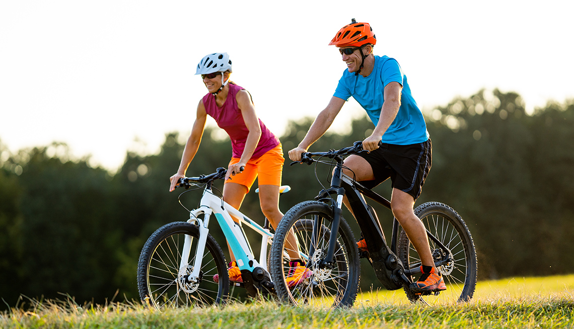Smiling sporty fit couple enjoying summer cycling day outdoors in rural landscape on electric mountain bikes shallow focus on man