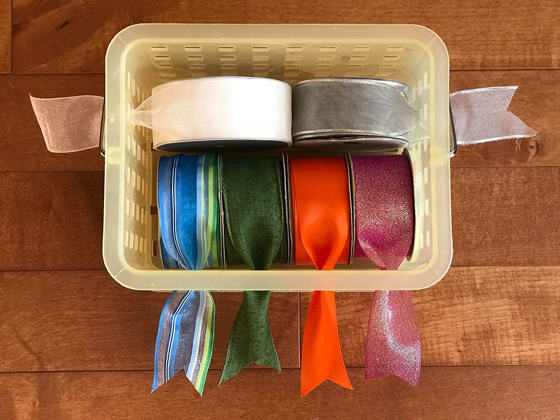 rolls of ribbon are store in a container that has holes on the sides that the ribbon can be pulled through