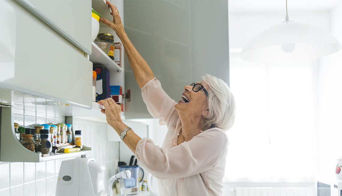 woman reaching for high item in kitchen cabinet