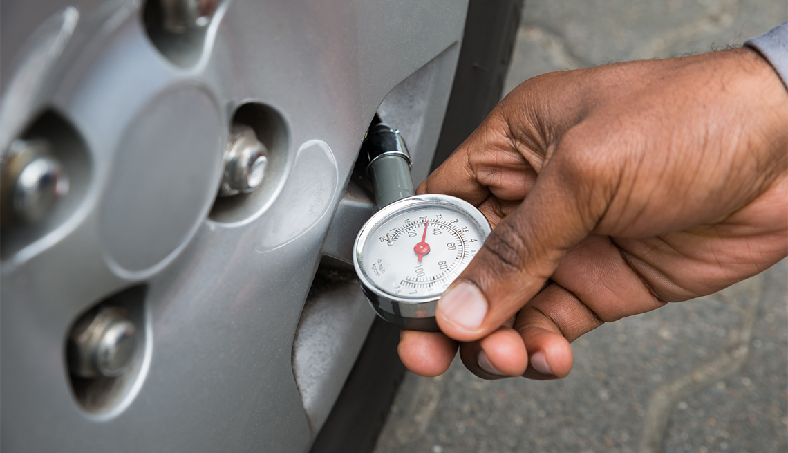 Persona revisa la presión de los neumáticos del auto