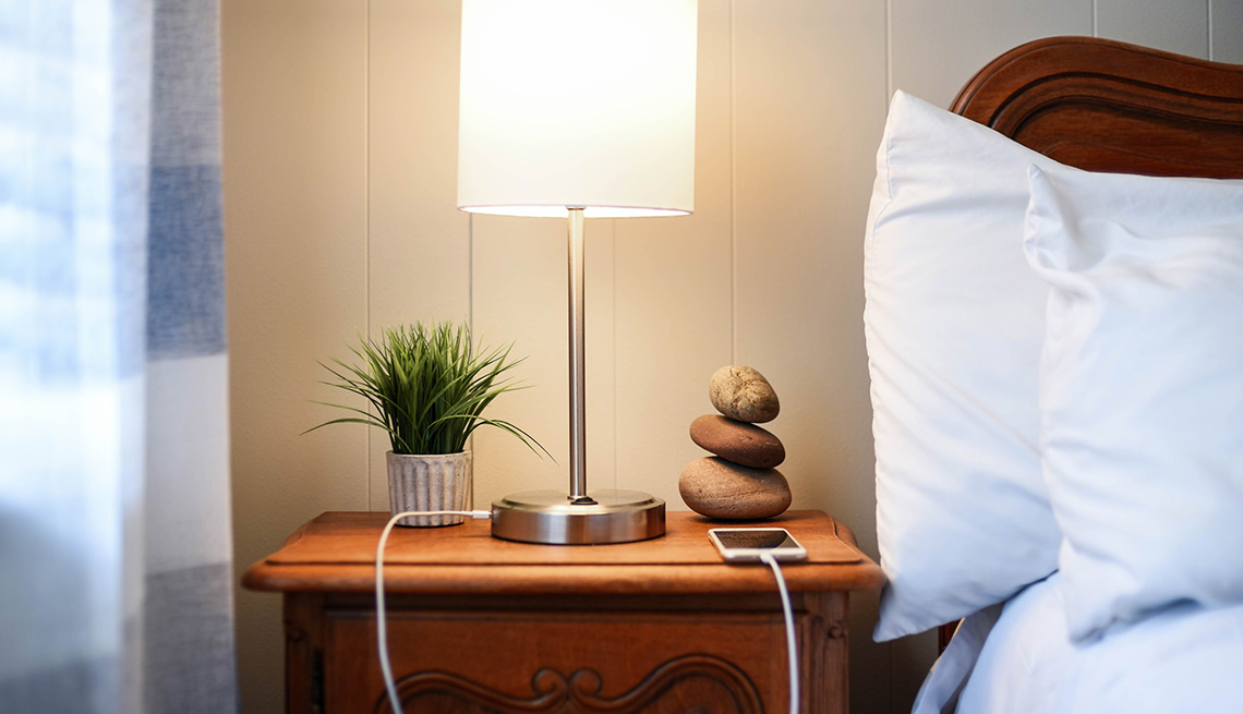 A smartphone plugged in to a plug located on the base of a lamp on a nightstand