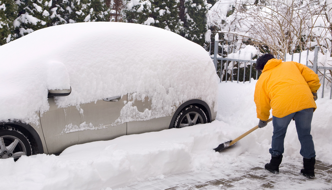Persona remueve la nieve con una pala alrededor de su auto