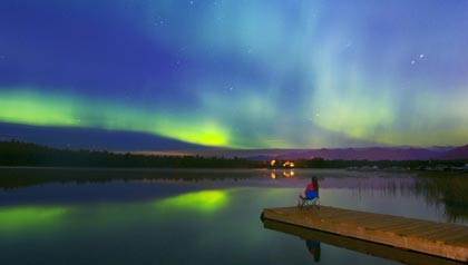 Woman at end of pier gazes at nothern lights 