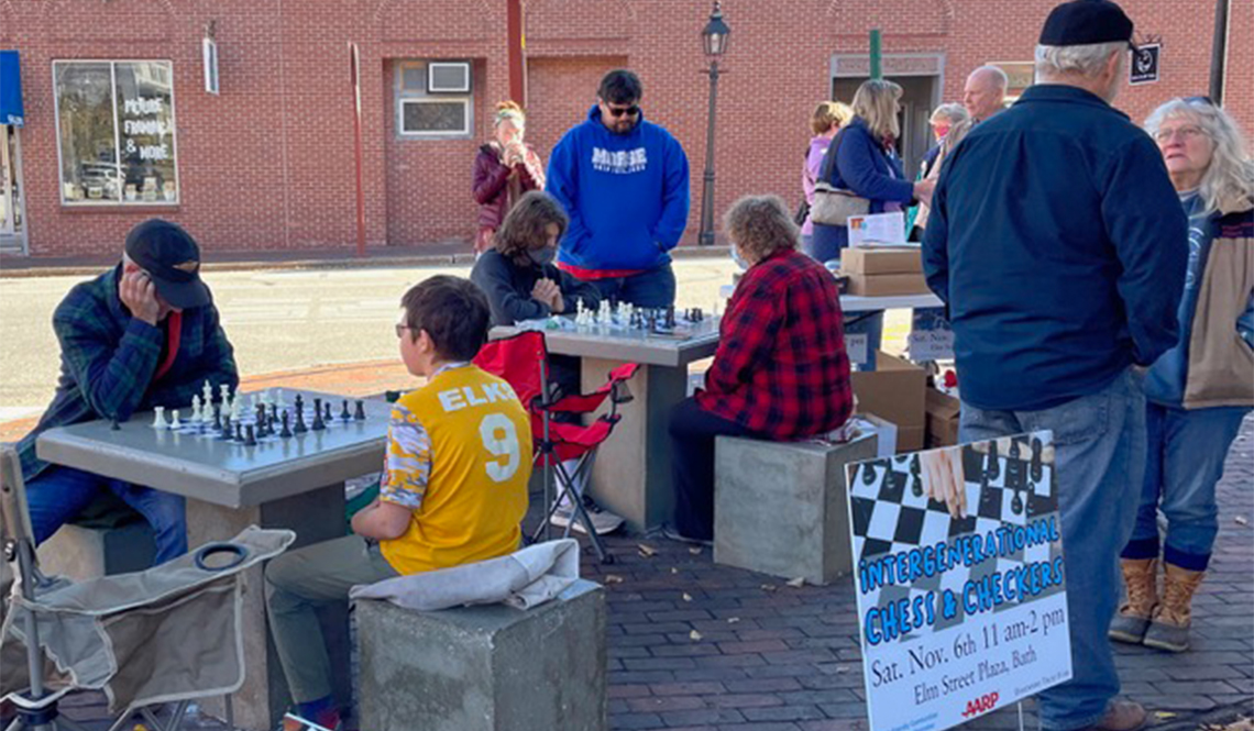 Children and adults play chess on outdoor tables