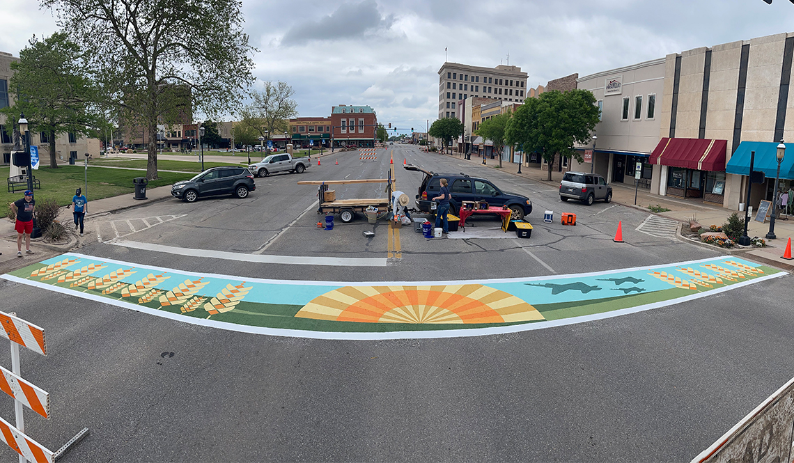 A painted crosswalk mural traversing a four-lane downtown roadway