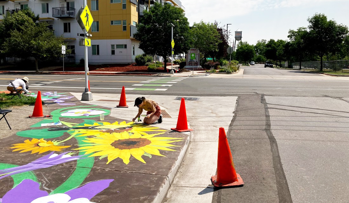 Volunteers paint giant sunflowers on a sidewalk corner