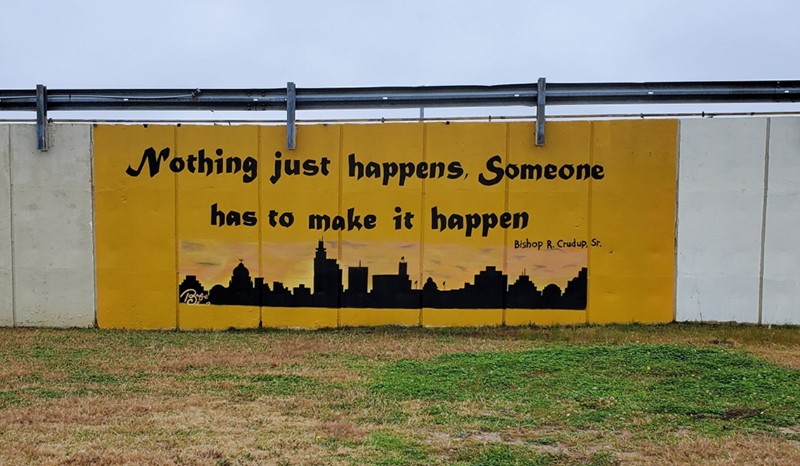 An orange and black mural says 'Nothing just happens. Someone has to make it happen."