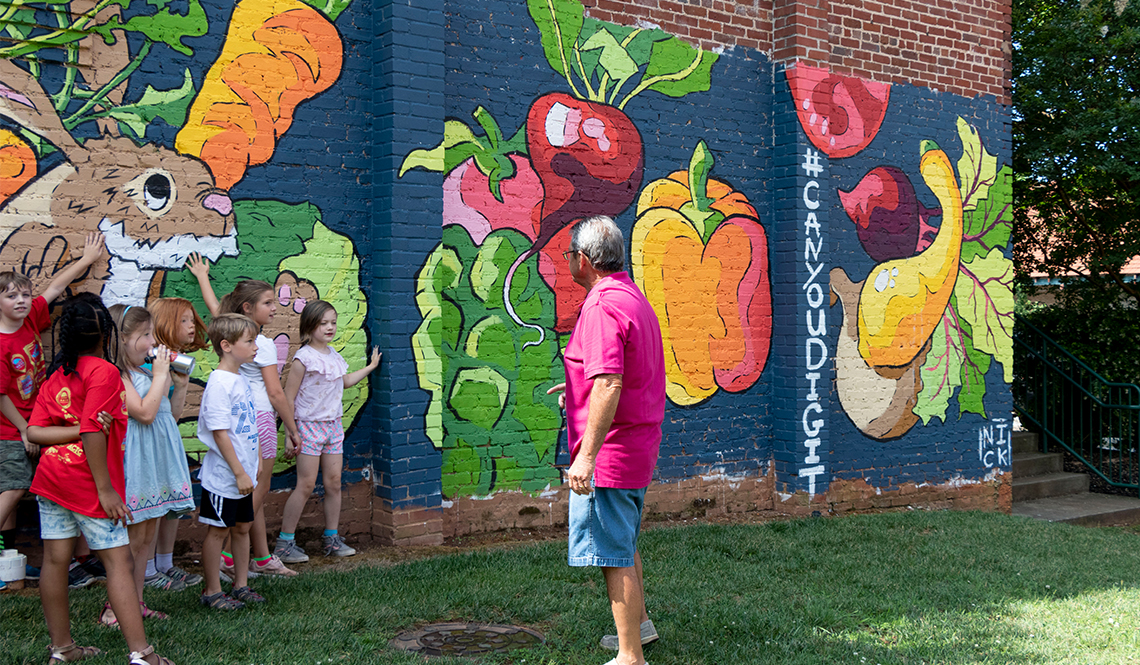 Children and a man stand near a mural featuring fruits, vegetables and a bunny