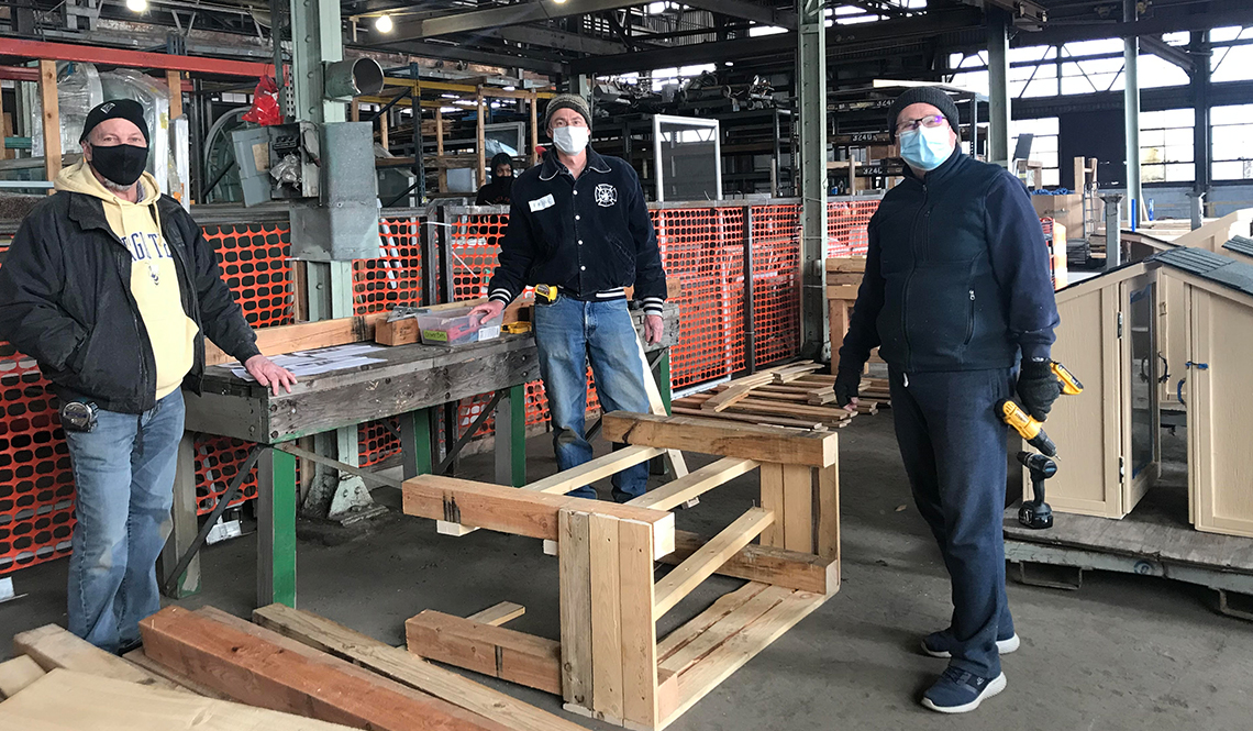 Three men pose in a warehouse where they are building raised-bed planters