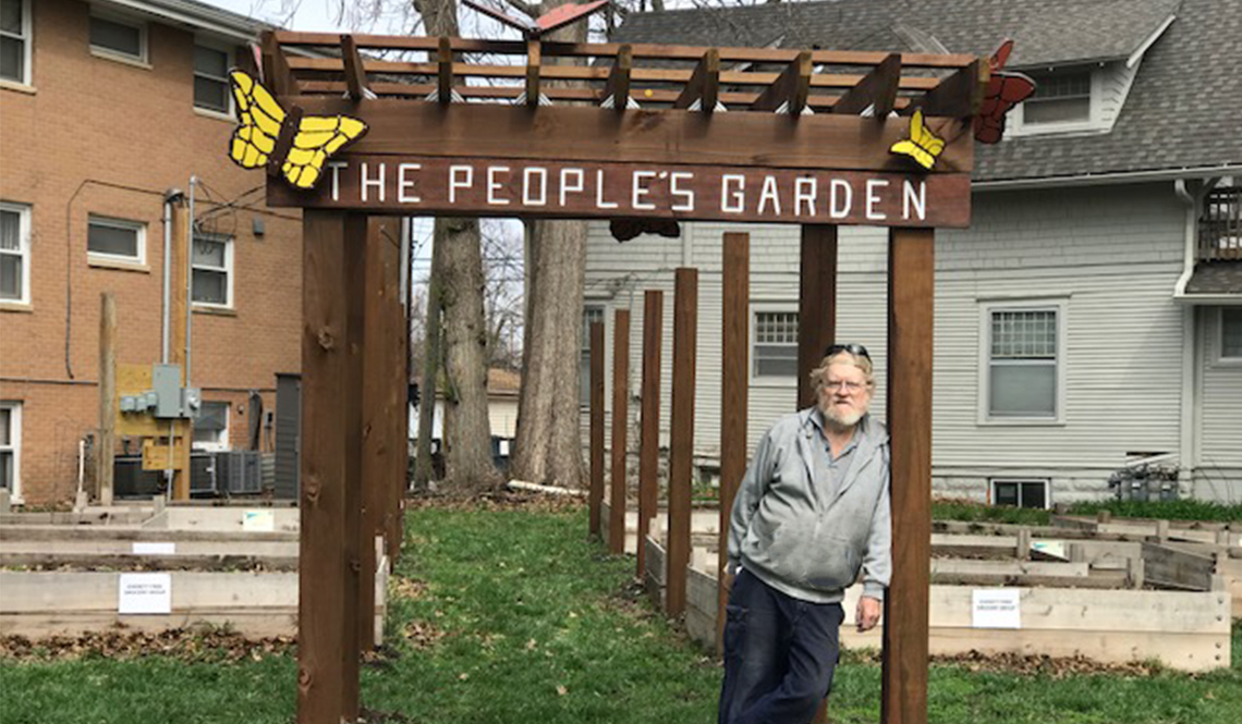 A man stands beneath a pergola decorated with butterfly art and the words The People's Garden