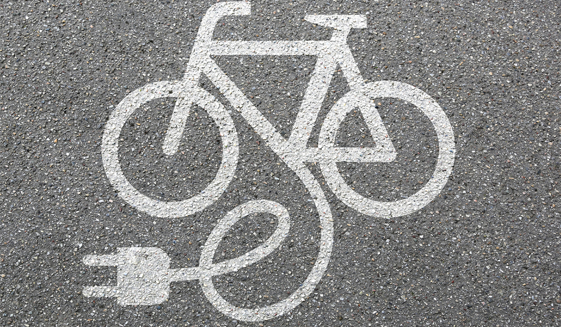 The image of a bicycle with an electric plug as seen stenciled on pavement with white paint.