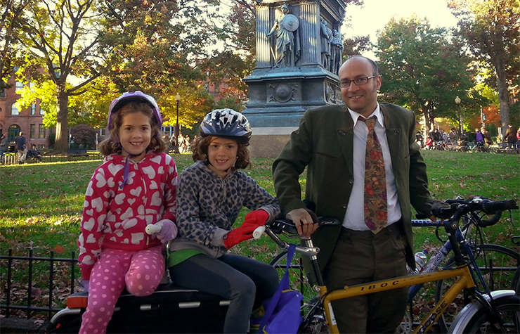 Un padre y sus hijas gemelas montan una bicicleta construida para tres.