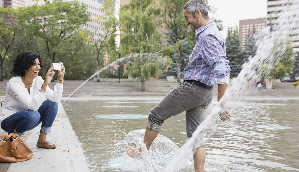 Woman Takes Man's Picture While He Stands In Public Fountain Splashing Water, Urban Setting, Buildings In Background, Water, In Livable Communities Slideshow