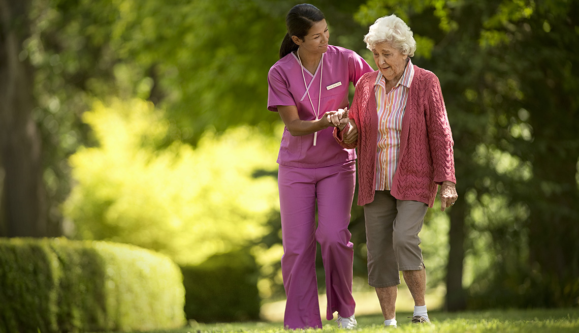Nurse Assists Elderly Woman To Walk Outdoors, Grass, Trees, Greenery, Nursing Home, AARP Livable Communities, Green House Nursing Home Concept