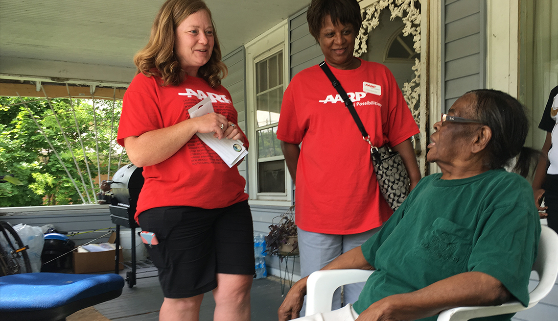 Two women representing AARP Michigan visit with a Flint resident who's sitting on her front porch.