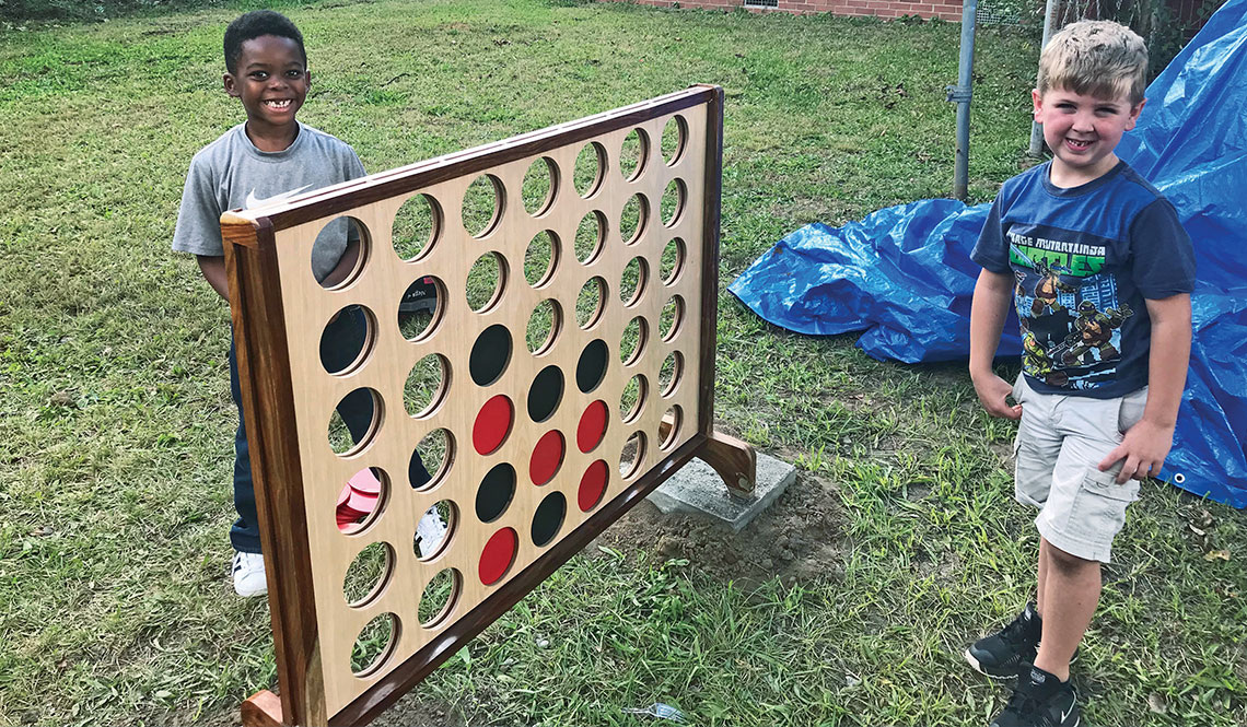 Two young boys stand next to a giant Connect4 game