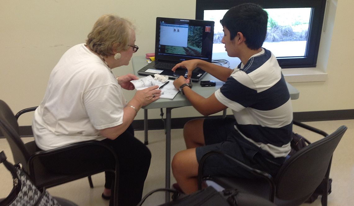 A teenage boy teaches an older woman how to use her digital camera