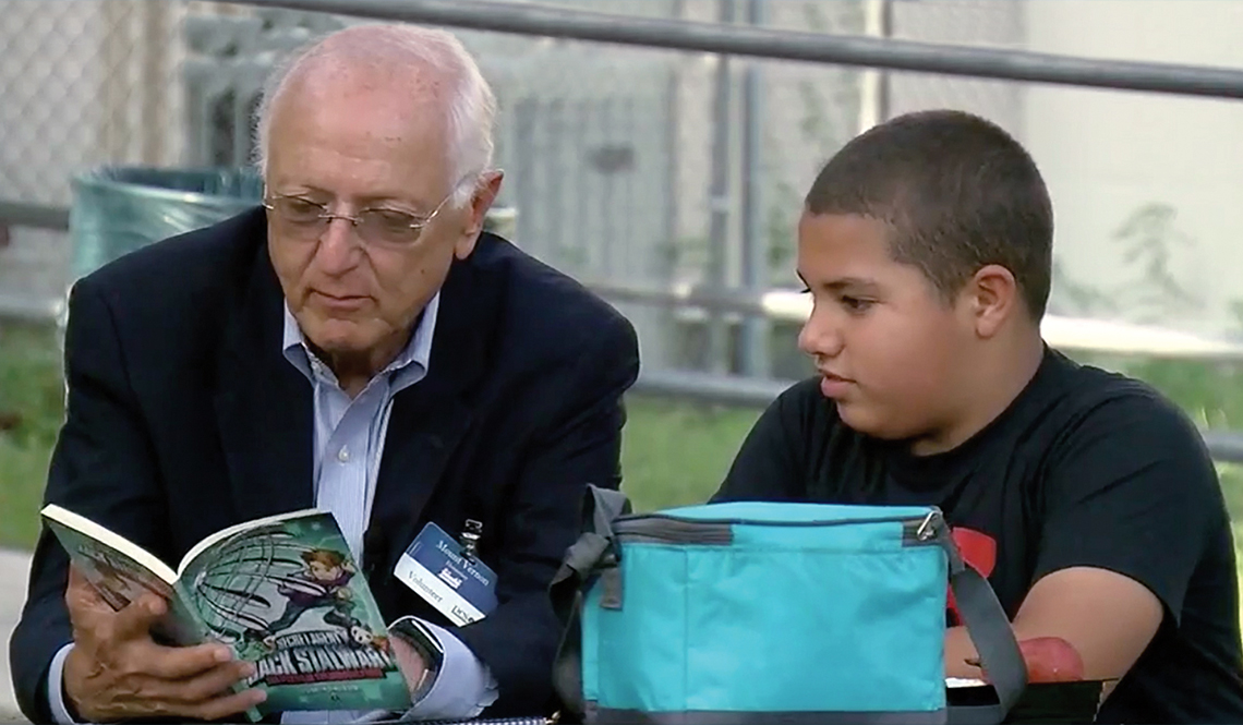 Volunteer Ron Diner reading a book with Davion, his young "lunch pal"