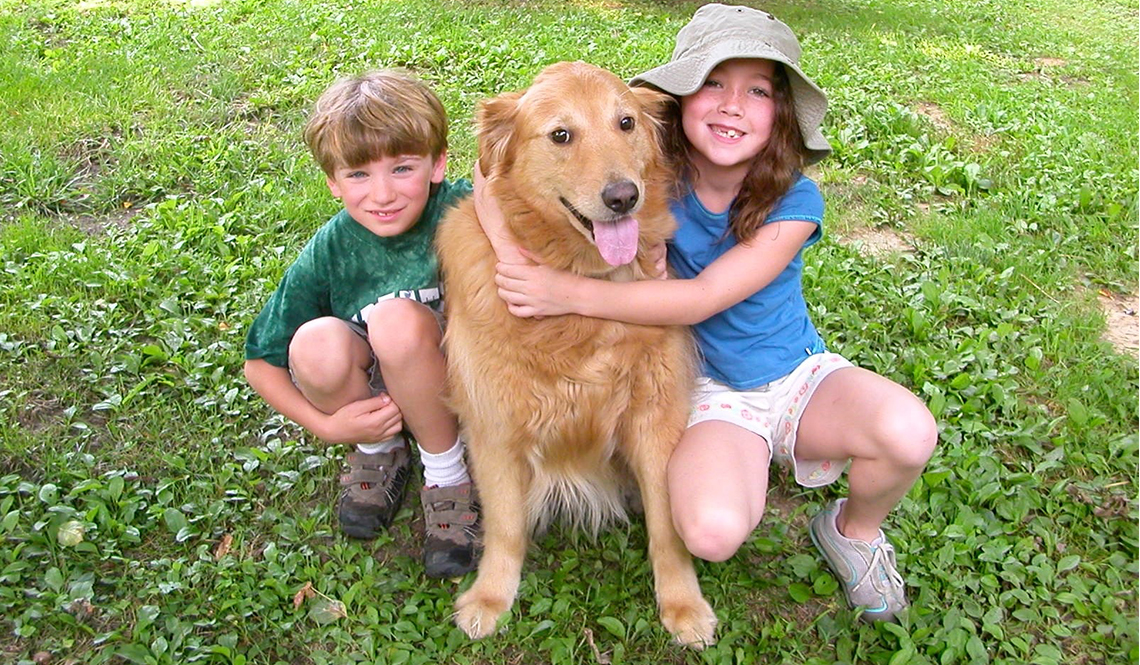 A young boy and girl pose with a happy Golden Retriever