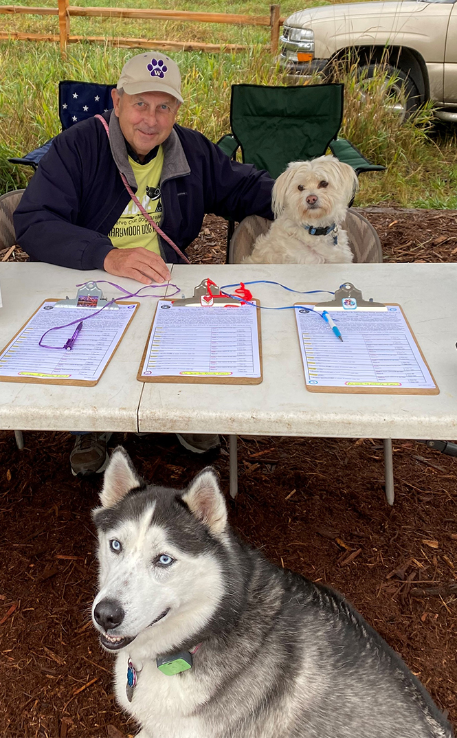 A man and two dogs staff the check-in table at a dog park event
