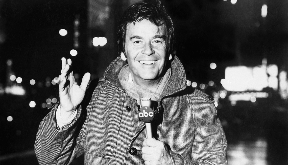 item 1 of Gallery image - Dick Clark waves to the camera he's facing while smiling and holding an ABC microphone