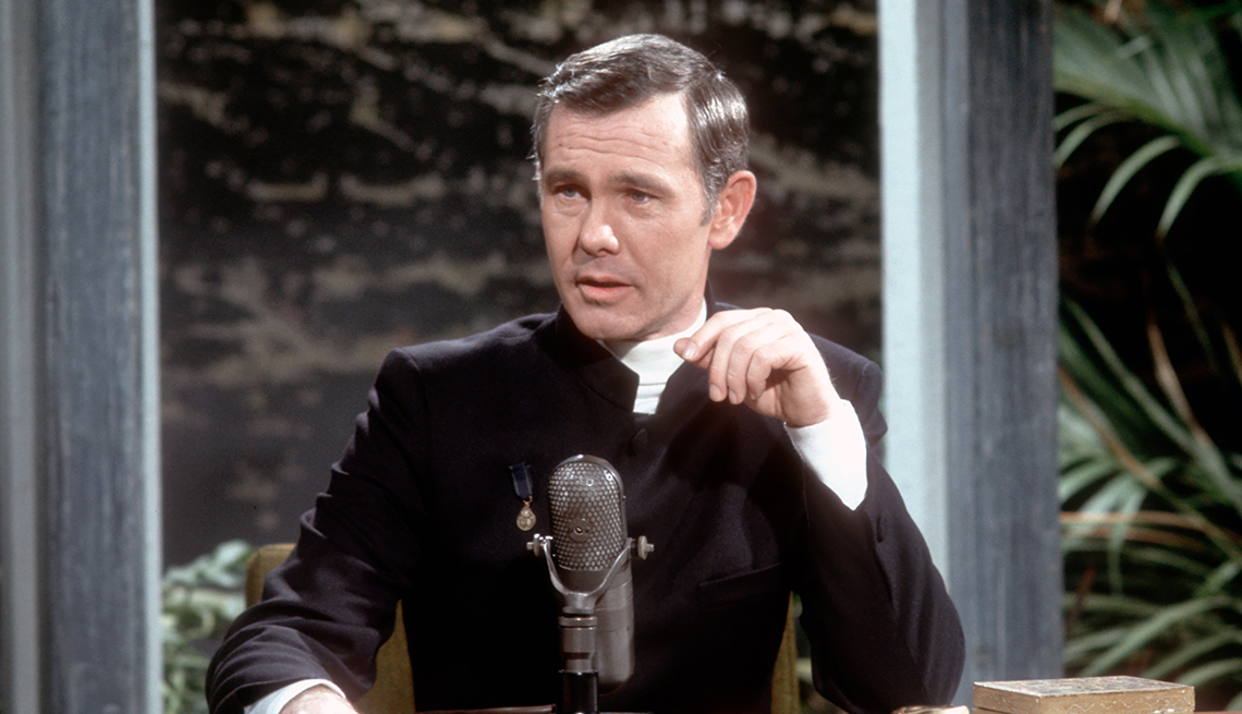 item 31 of Gallery image - Johnny Carson sits behind a microphone with a plant behind him on the set of The Tonight Show Starring Johnny Carson