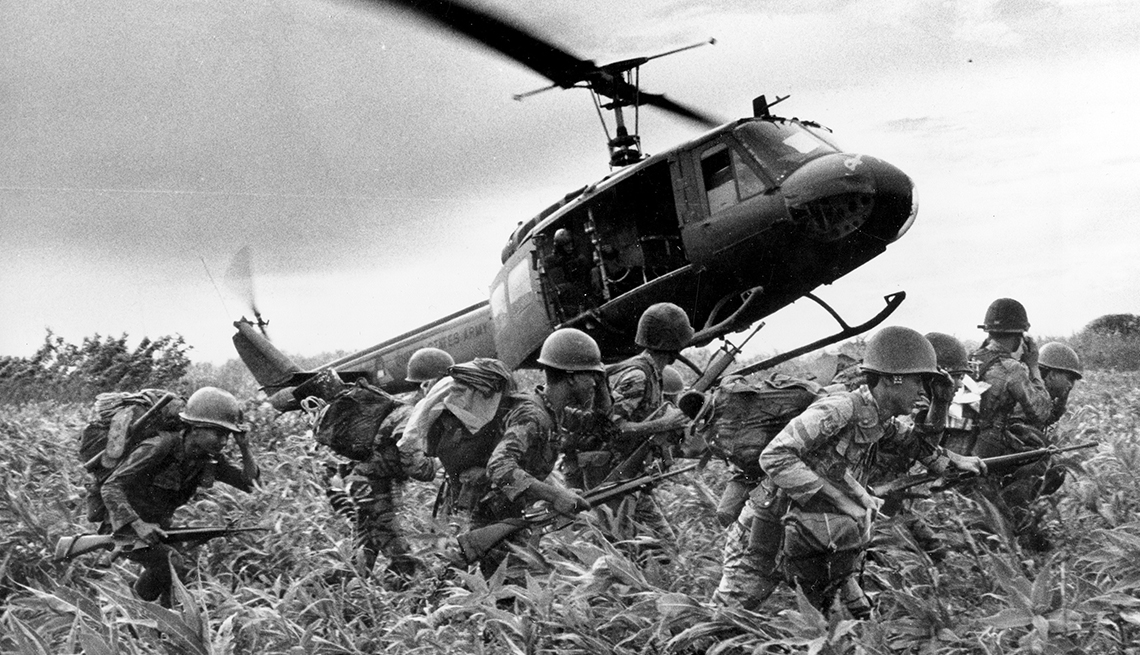 item 2 of Gallery image - A helicopter flies low to the ground near soldiers during the Vietnam War
