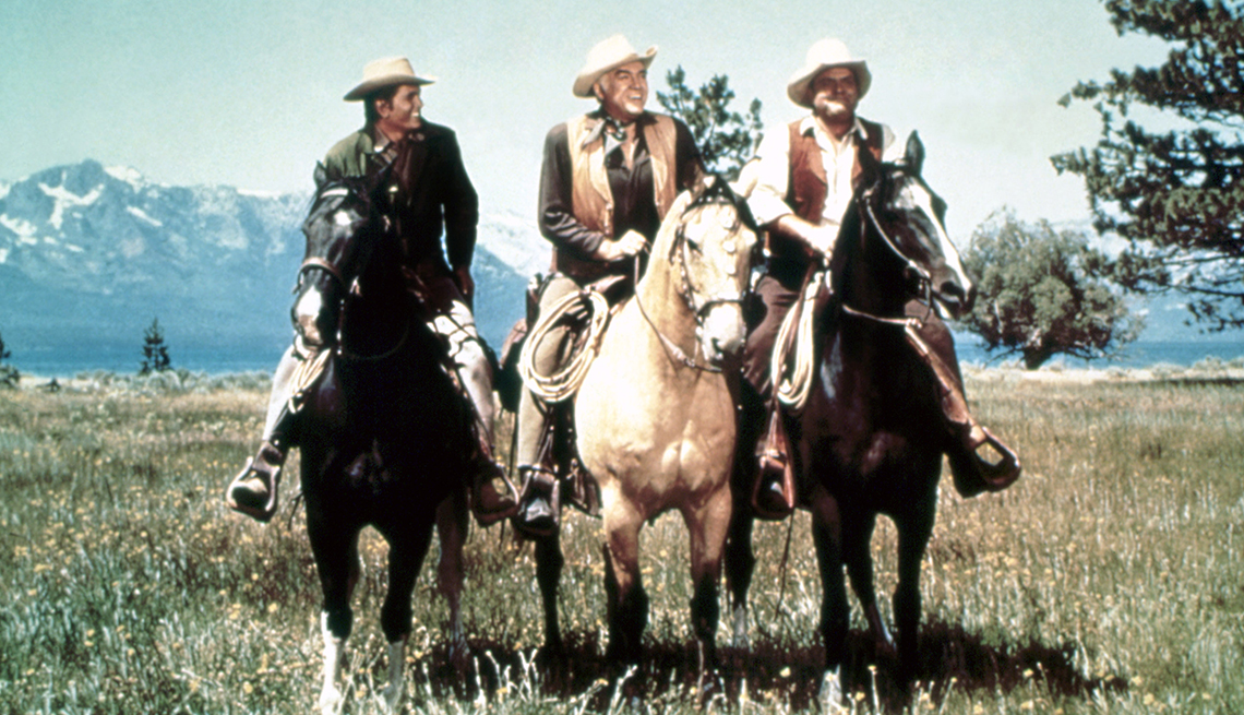 item 16 of Gallery image - 'Bonanza' cast members Michael Landon, Lorne Greene and Dan Blocker pose in cowboy costumes on horses in a green field with mountains in the background
