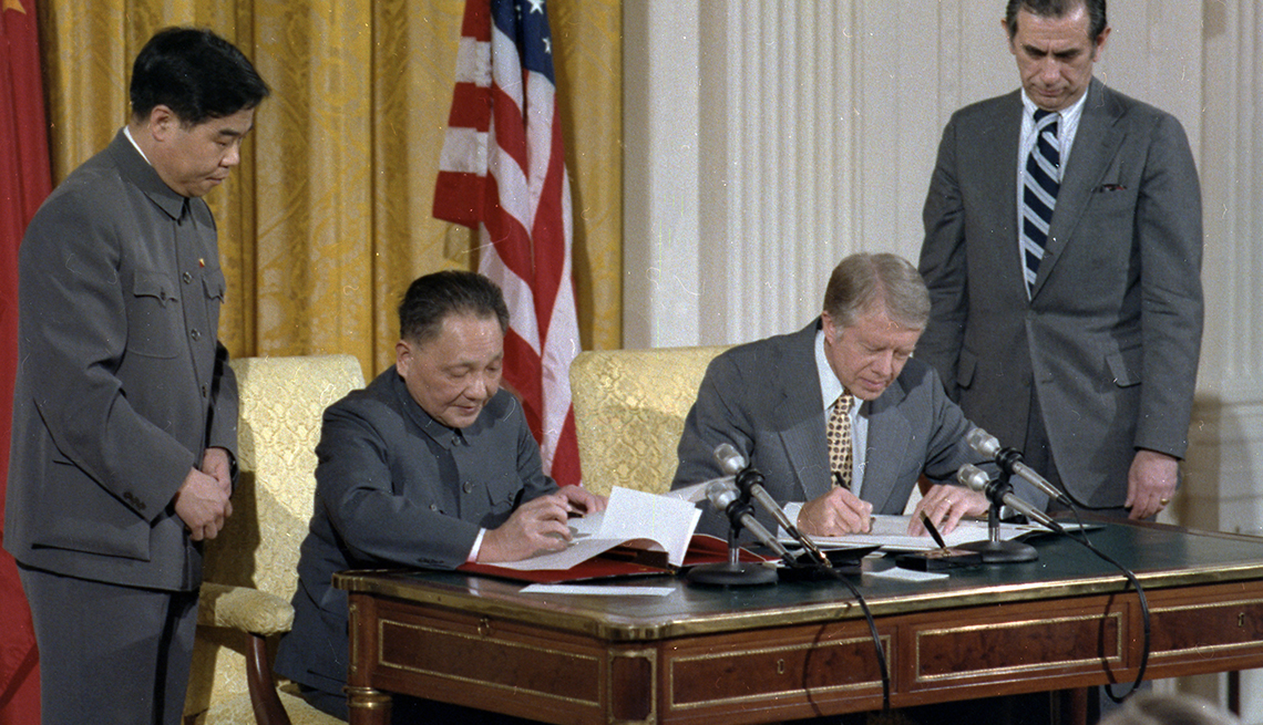 item 3 of Gallery image - A uniformed Vice Premier Deng Xiaoping and a gray-suited President Jimmy Carter sign papers at a desk while a Chinese and an American official look on