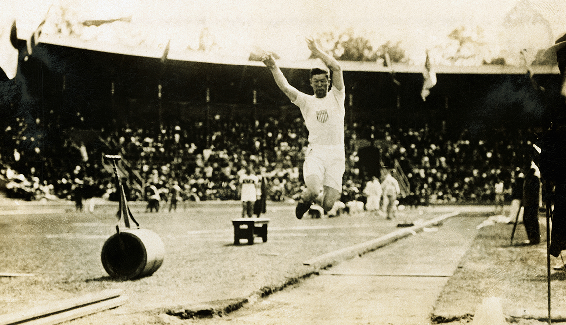 A sepia tone photo shows Jim Thorpe in mid-jump during a long jump event at the Olympics