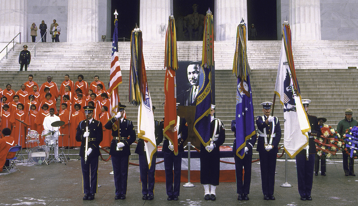 Eight people in uniform hold flags in front of a choir dressed in red on the steps of the Lincoln Memorial