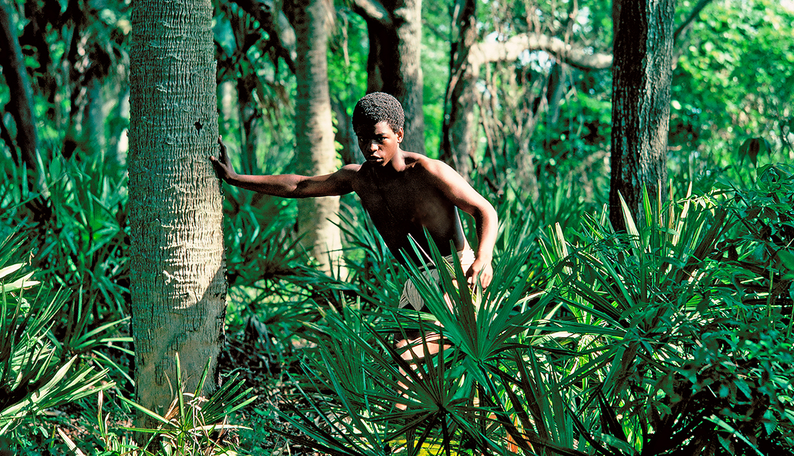LeVar Burton playing young Kunta Kinte in the television film roots runs through a lush forest while shirtless and wearing beige pants