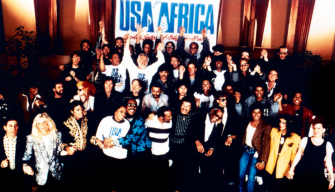 A host of famous performers smiles in front of a banner that reads 'USA for Africa' in big, blue letters