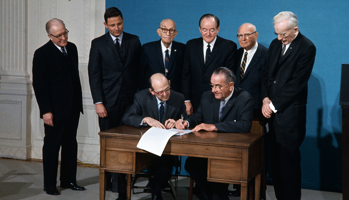 item 19 of Gallery image - Lawson Knott of the General Services Administration and a number of other men in suits look on while President Lyndon Johnson signs a document