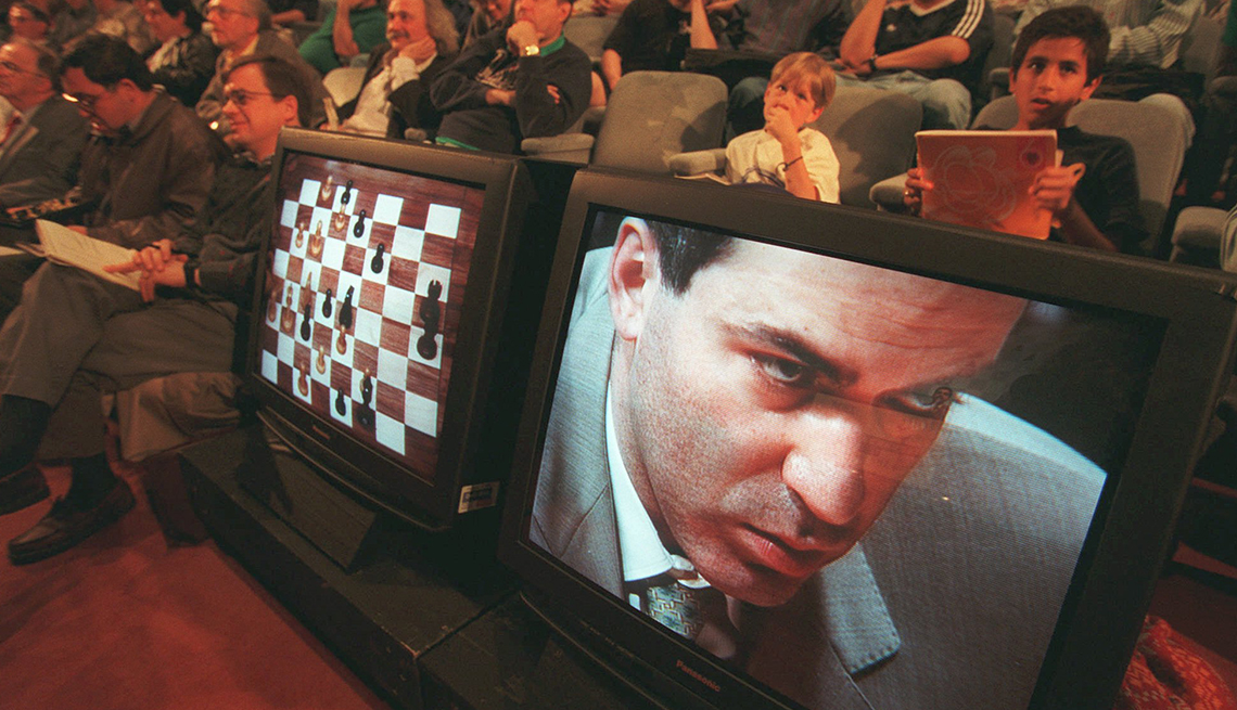 item 12 of Gallery image - video screens in front of seated people show Garry Kasparov to the right and a chessboard to the left