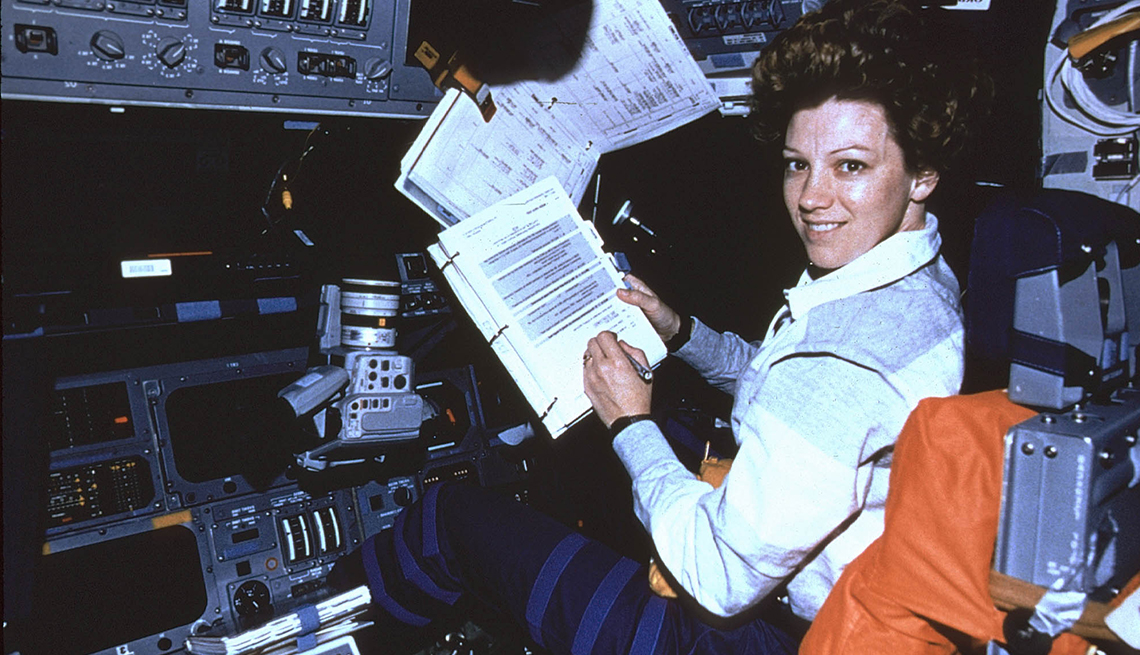 item 26 of Gallery image - Eileen Collins looks at the camera while handling paperwork, seated in a cockpit