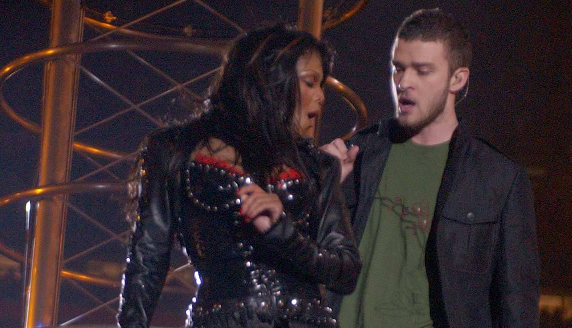 item 28 of Gallery image - Janet Jackson is dressed in black leather and Justin Timberlake is wearing a black jacket and green t-shirt while they hold microphones and sing together in front of a scaffold