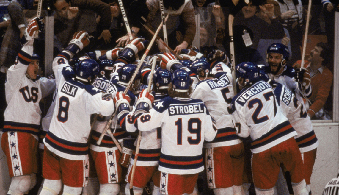 item 7 of Gallery image - American hockey players are facing the glass while they wave their sticks in celebration