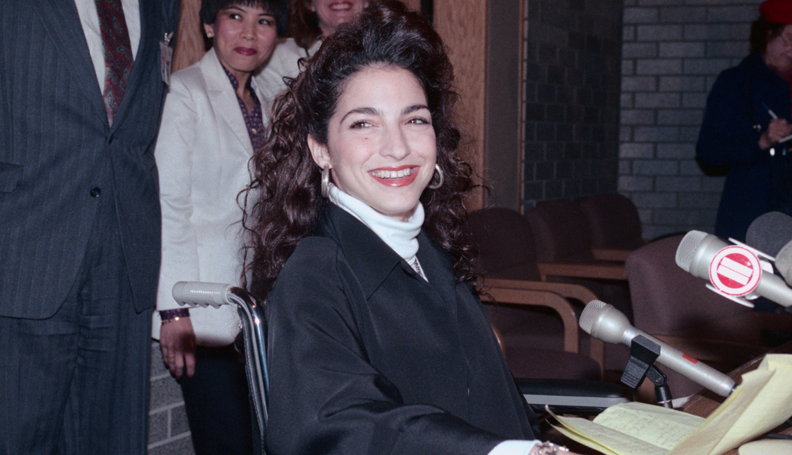 item 12 of Gallery image - pop star gloria estefan in a black robe and a wheelchair in front of several microphones