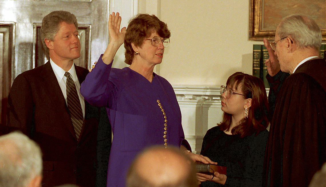 item 20 of Gallery image - janet reno is wearing a purple outfit with one hand raised as she's sworn in as attorney general with a child looking on and former president bill clinton in the background