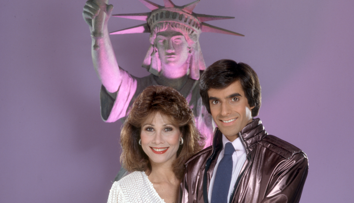 item 23 of Gallery image - Guest star Michele Lee and illusionist David Copperfield pose in front of a small Statue of Liberty 
